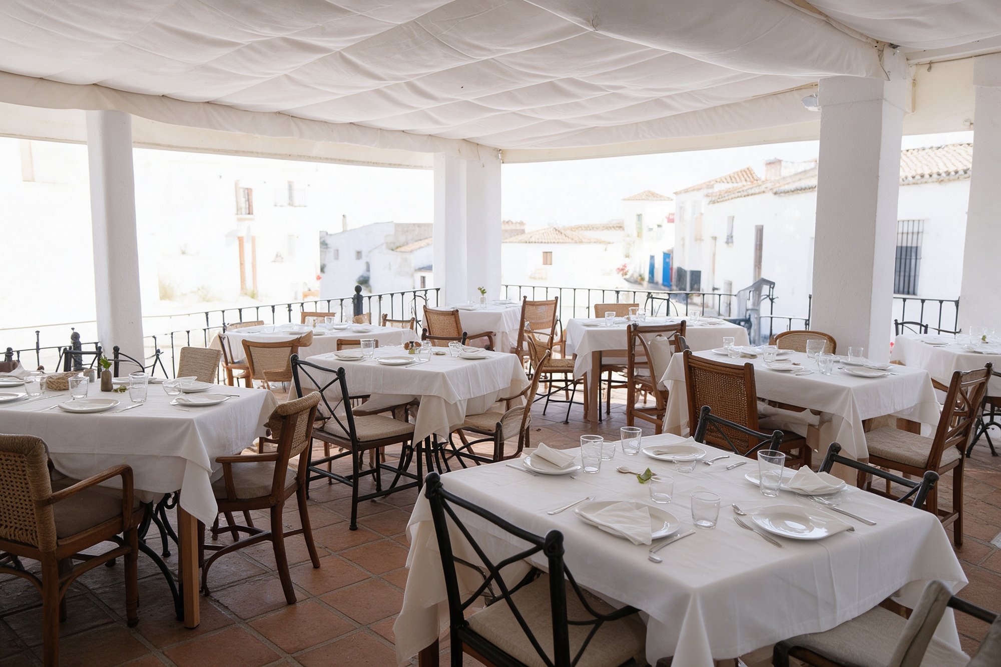 Terraza cubierta del restaurante con tejadillo de lona blanca, mesas vestidas con manteles y vistas a las casas blancas del pueblo